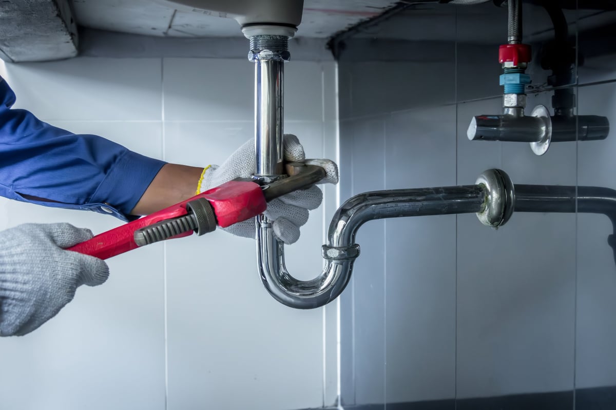 Plumber using a pipe wrench to repair the drain under a kitchen sink